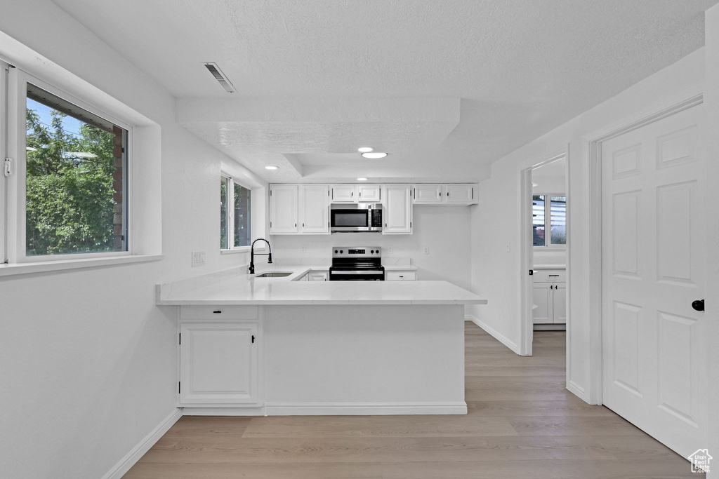Kitchen with appliances with stainless steel finishes, a sink, a textured ceiling, light countertops, and light wood-type flooring