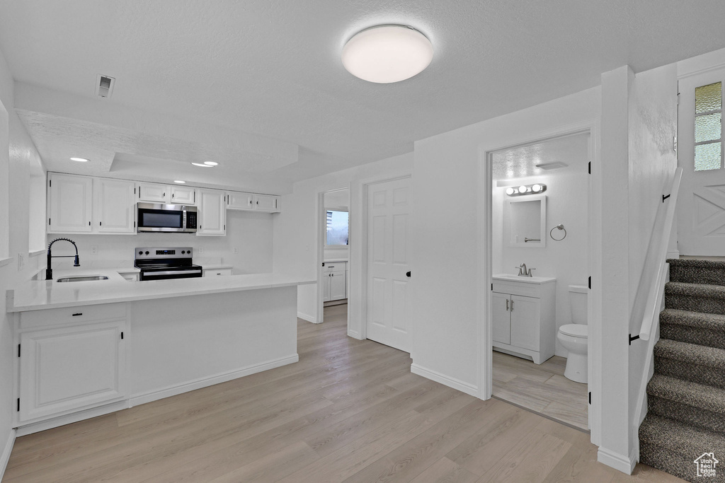 Kitchen with appliances with stainless steel finishes, light wood-type flooring, a sink, light countertops, and recessed lighting