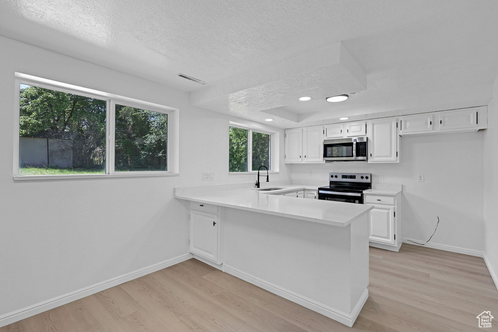 Kitchen with stainless steel appliances, a sink, light wood-style flooring, a textured ceiling, and white cabinetry