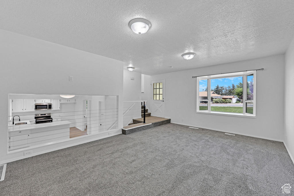 Carpeted spare room featuring a sink, a textured ceiling, baseboards, and stairway