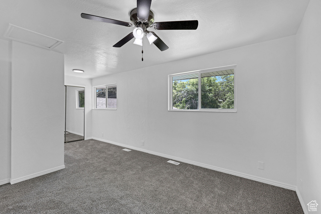 Unfurnished room with dark carpet, ceiling fan, baseboards, and a textured ceiling