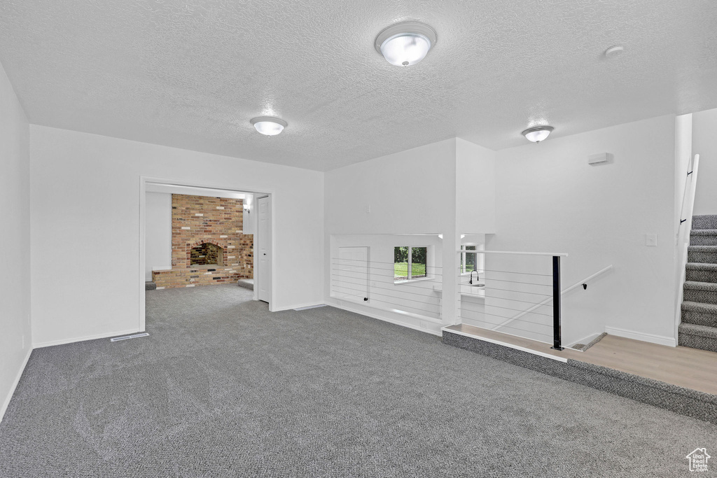 Carpeted empty room featuring a textured ceiling, baseboards, a fireplace, and stairway