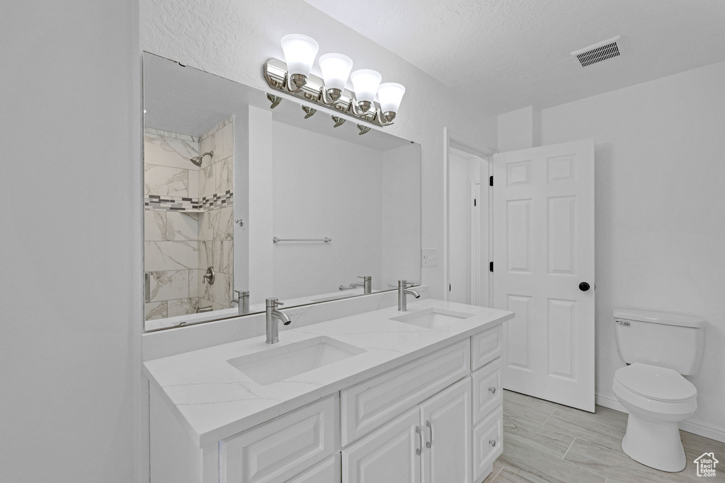 Bathroom with double vanity, toilet, tiled shower, and a textured ceiling