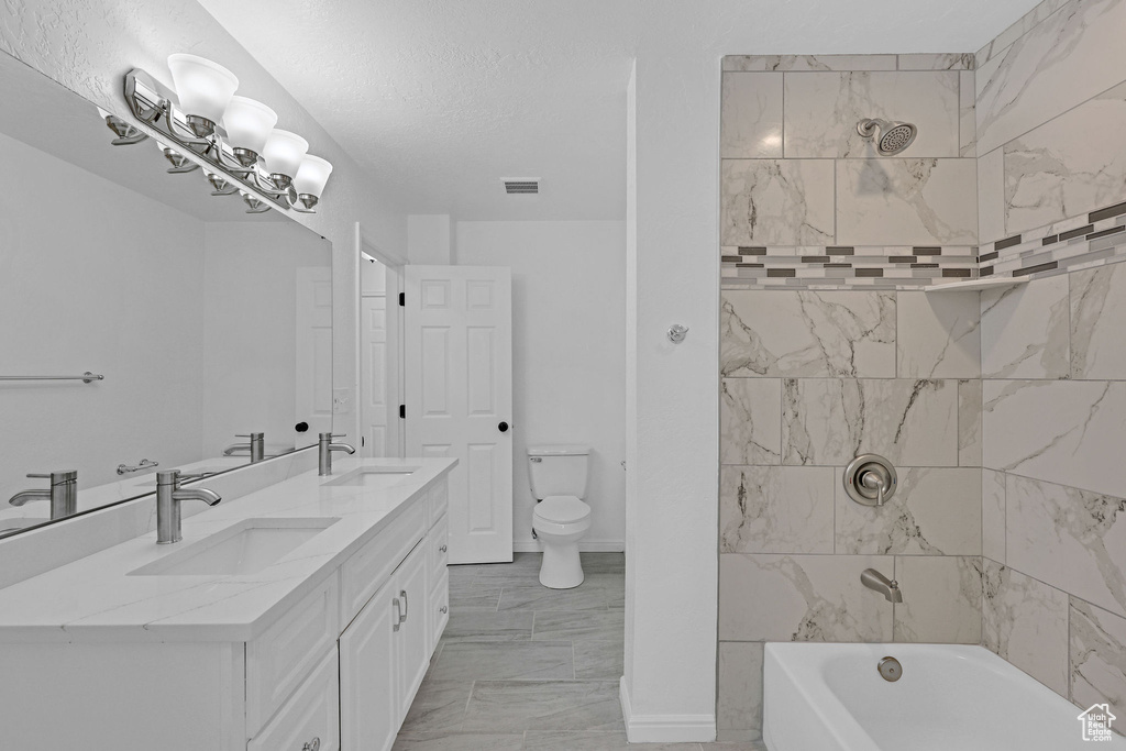 Full bath featuring marble look tiles, double vanity, toilet, and washtub / shower combination