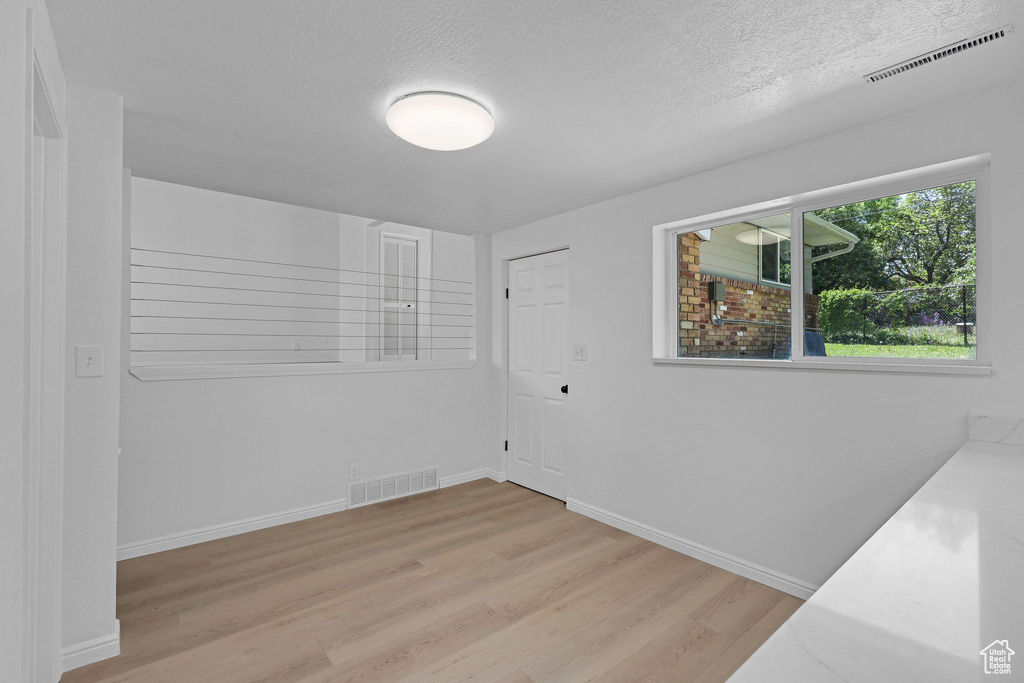 Spare room featuring light wood-type flooring, a textured ceiling, and baseboards