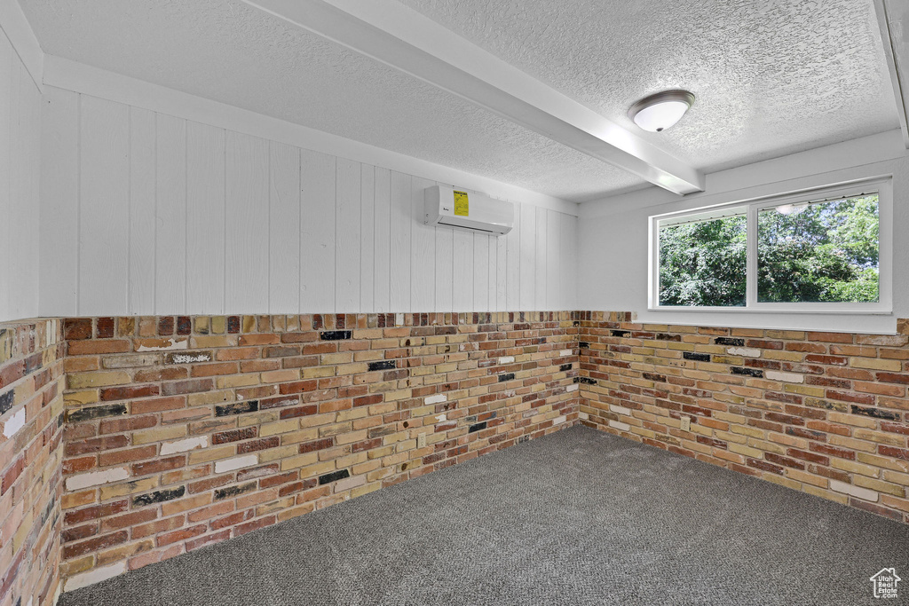 Carpeted spare room featuring a wall unit AC and a textured ceiling