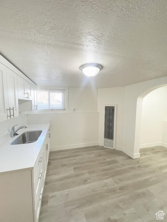 Kitchen featuring a sink, a textured ceiling, light wood finished floors, arched walkways, and light countertops