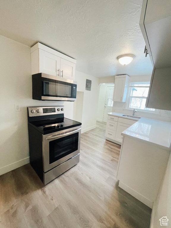 Kitchen with stainless steel appliances, baseboards, light wood-style flooring, white cabinetry, and a textured ceiling