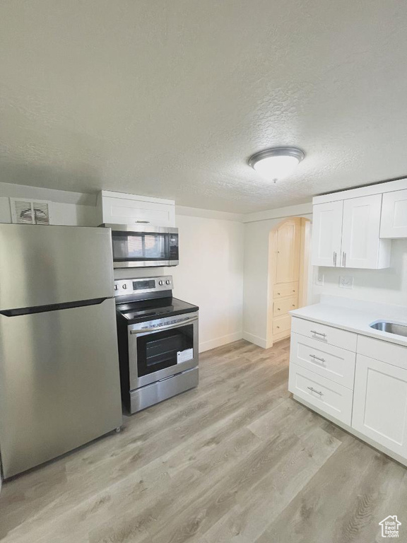Kitchen featuring appliances with stainless steel finishes, light wood finished floors, white cabinetry, a textured ceiling, and light countertops