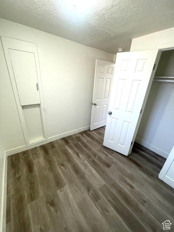 Unfurnished bedroom with a textured ceiling, dark wood-style floors, baseboards, and a closet