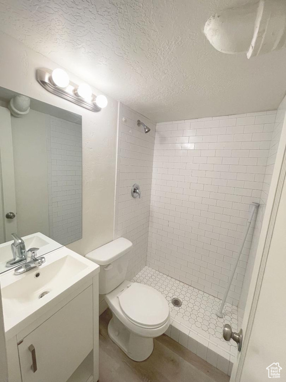 Bathroom featuring tiled shower, vanity, a textured ceiling, and toilet