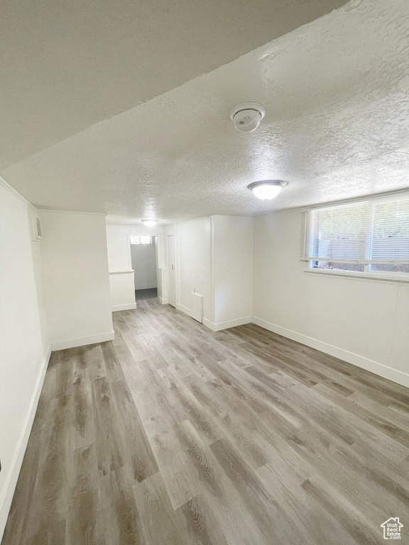Basement with wood finished floors, baseboards, and a textured ceiling