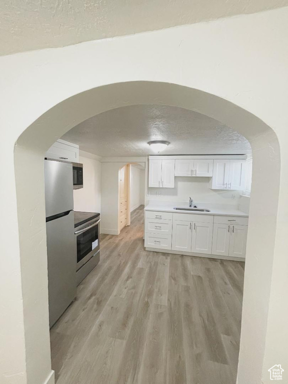Kitchen with appliances with stainless steel finishes, a sink, light wood-style flooring, white cabinets, and arched walkways