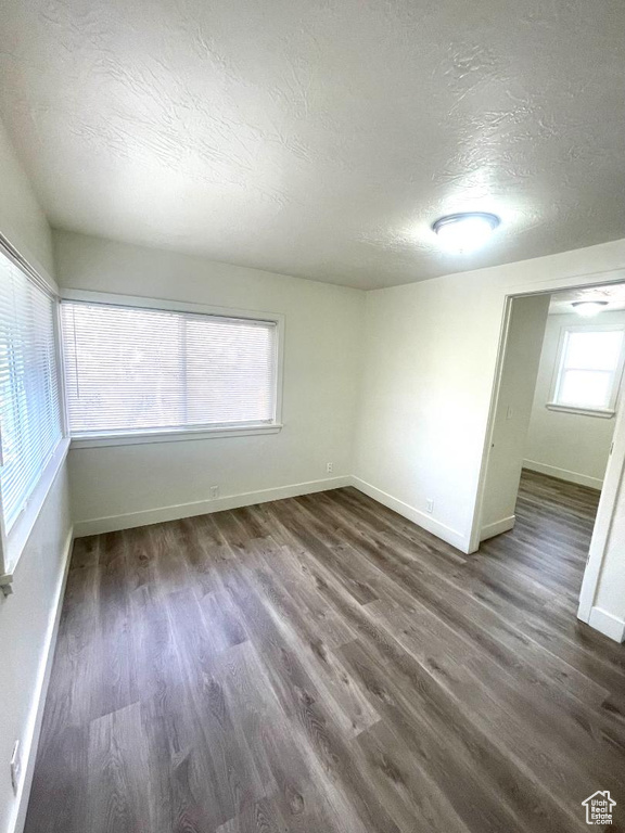 Empty room with a textured ceiling, baseboards, and dark wood-type flooring
