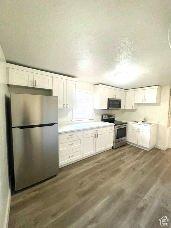 Kitchen with appliances with stainless steel finishes, wood finished floors, white cabinets, a sink, and a textured ceiling