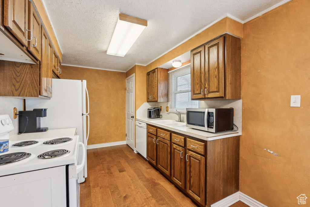 Kitchen with white appliances, a sink, brown cabinets, light wood-type flooring, and baseboards