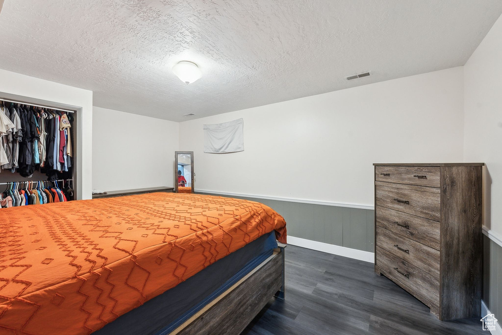Bedroom with dark wood finished floors, a wainscoted wall, a textured ceiling, a closet, and baseboards