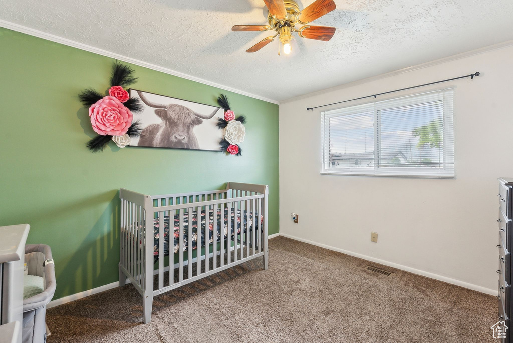 Bedroom featuring a textured ceiling, a crib, crown molding, carpet floors, and baseboards