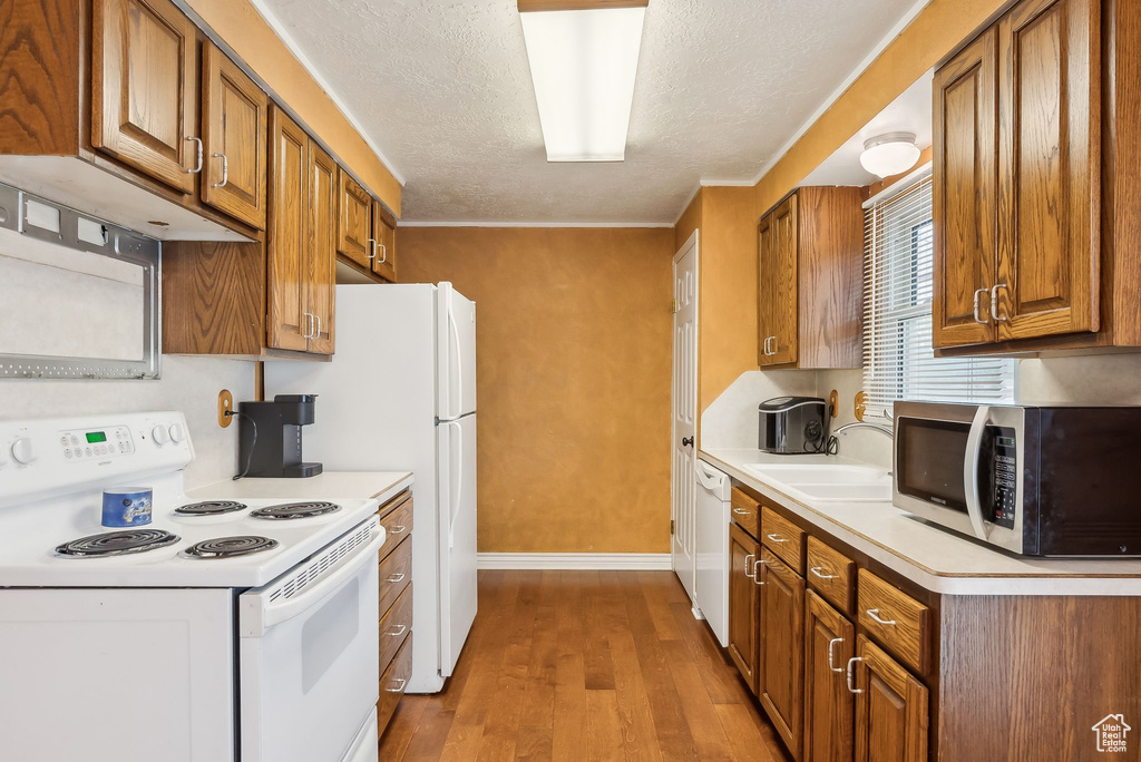 Kitchen featuring white appliances, a sink, light wood-style floors, brown cabinets, and a textured ceiling