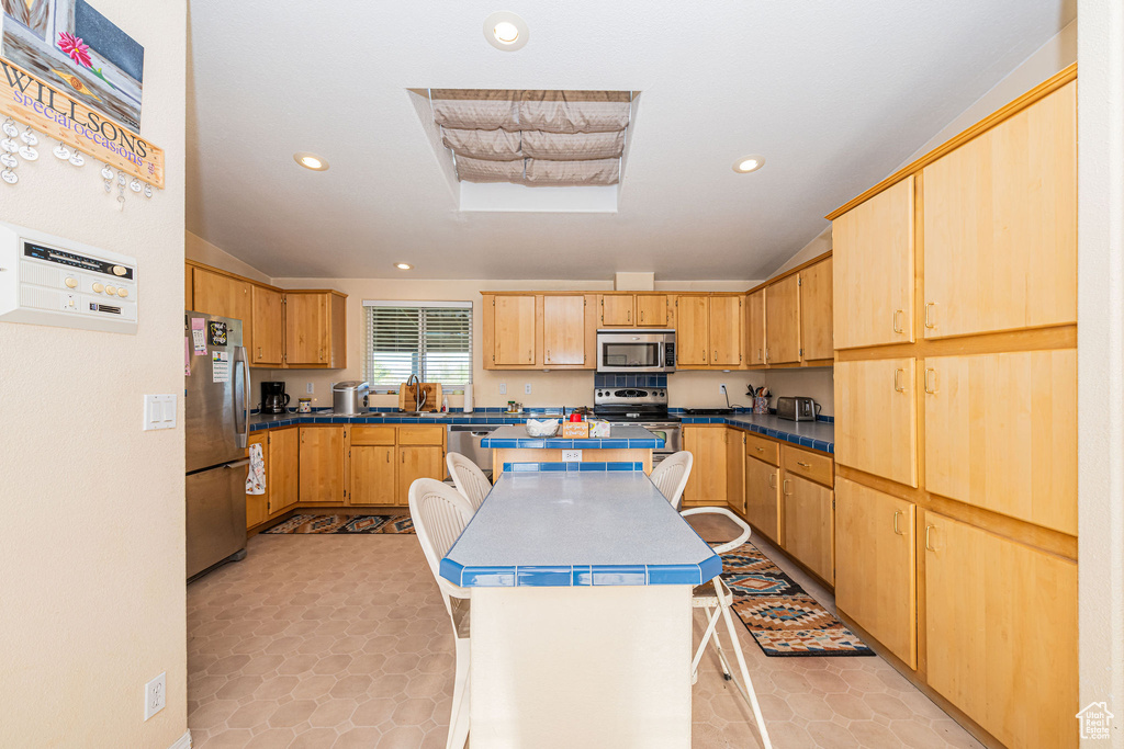 Kitchen with appliances with stainless steel finishes, a center island, recessed lighting, light brown cabinetry, and a breakfast bar area