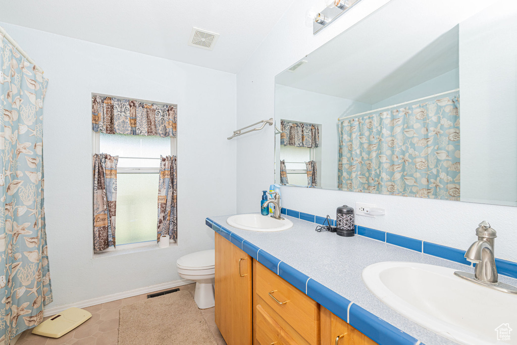Bathroom featuring double vanity, toilet, and baseboards