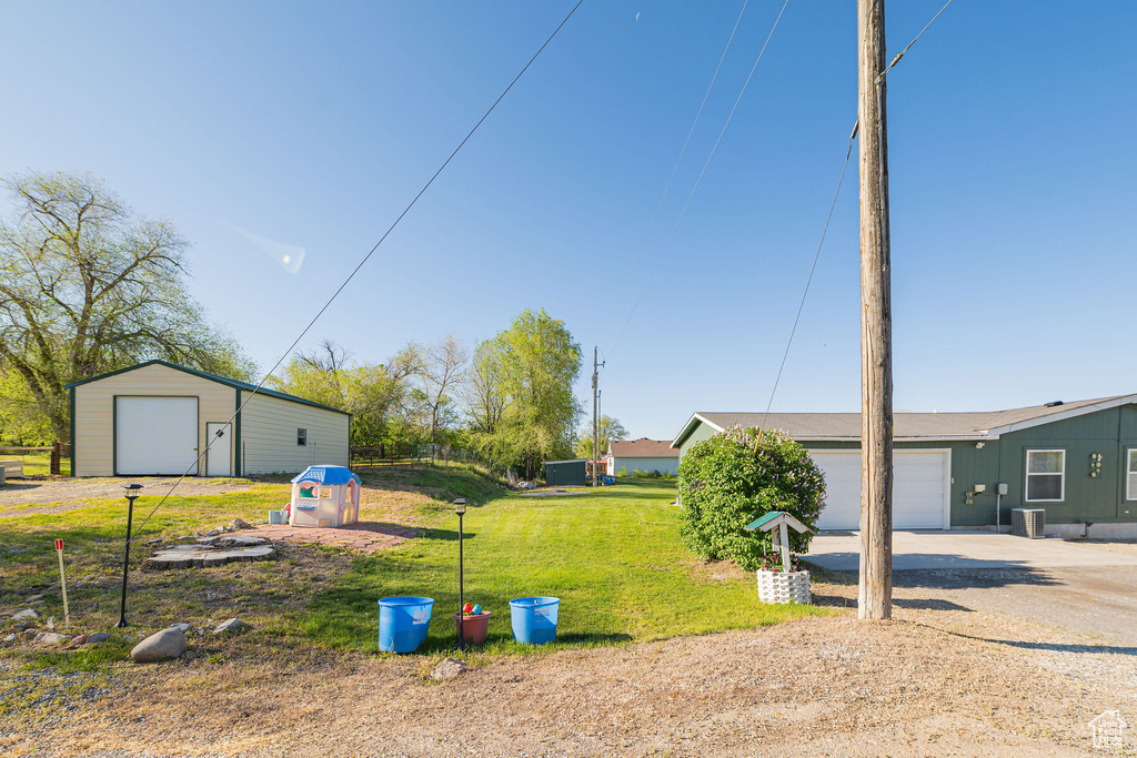 View of green lawn featuring driveway, an attached garage, an outdoor structure, and central AC unit