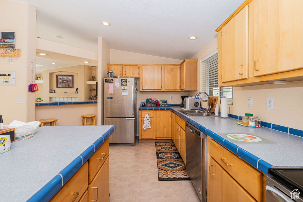 Kitchen with appliances with stainless steel finishes, a sink, lofted ceiling, recessed lighting, and tile countertops