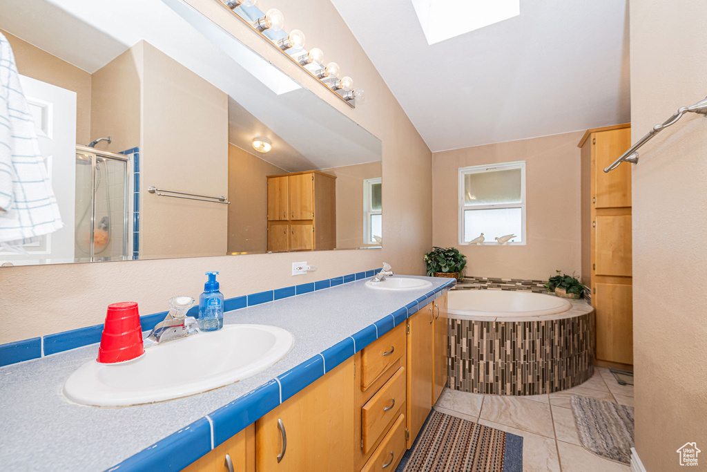 Bathroom featuring a skylight, a bath, double vanity, a stall shower, and tile patterned floors