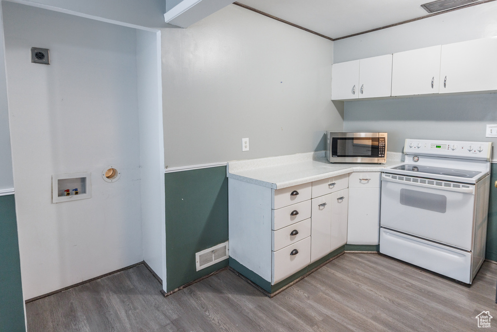 Kitchen featuring white range with electric stovetop, stainless steel microwave, wood finished floors, light countertops, and white cabinets