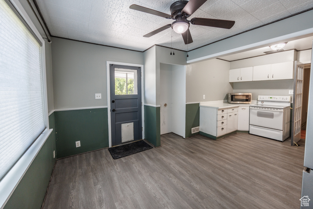 Kitchen with electric range, stainless steel microwave, wood finished floors, light countertops, and white cabinetry