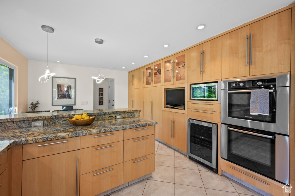 Kitchen with appliances with stainless steel finishes, beverage cooler, dark stone counters, light tile patterned floors, and pendant lighting