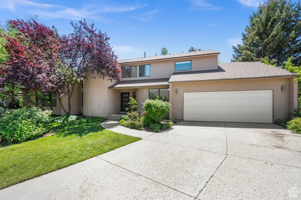 View of front of house featuring a garage, concrete driveway, a shingled roof, and a front lawn