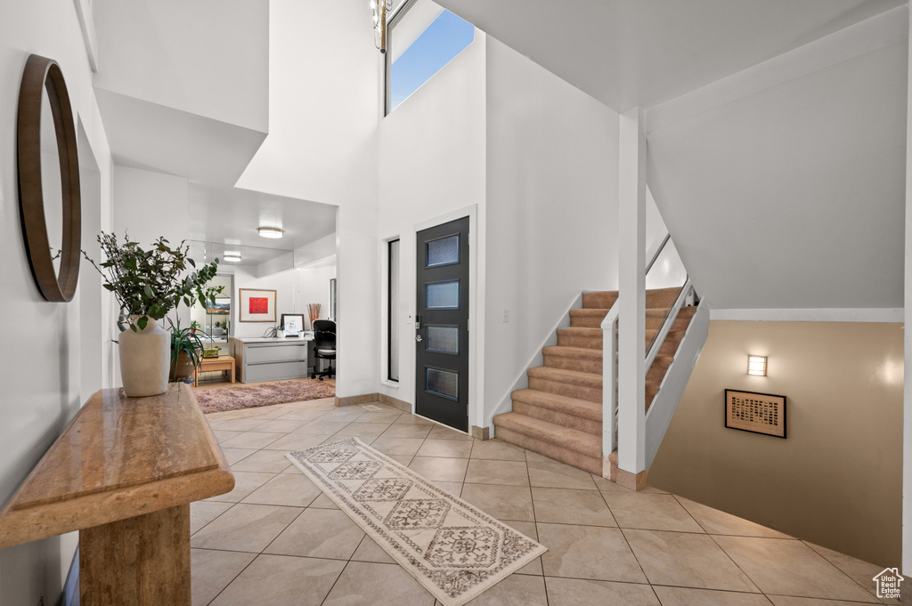 Foyer entrance featuring a high ceiling, light tile patterned flooring, stairway, and baseboards