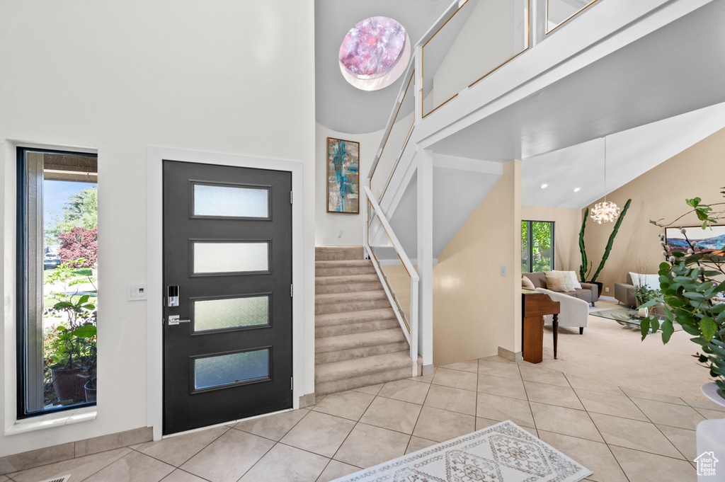 Entrance foyer with a towering ceiling, light tile patterned floors, stairway, and light colored carpet