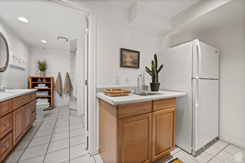 Kitchen featuring freestanding refrigerator, a sink, light countertops, light tile patterned floors, and recessed lighting