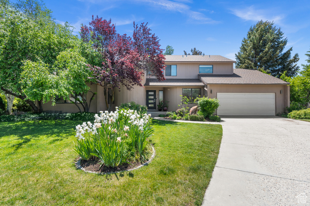 View of front of home with a garage, concrete driveway, a front yard, and roof with shingles