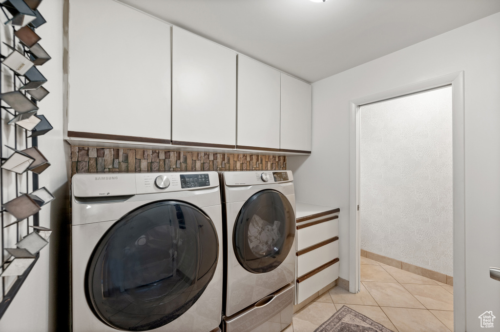 Laundry area with cabinet space, separate washer and dryer, light tile patterned floors, and baseboards