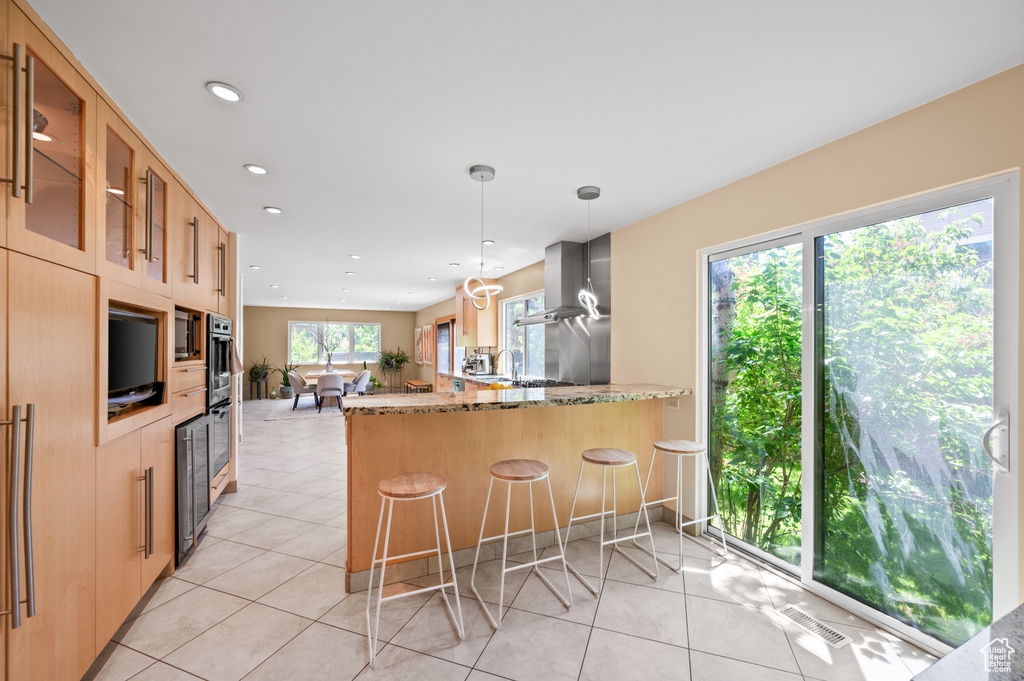 Kitchen with light stone countertops, wall chimney exhaust hood, glass insert cabinets, a peninsula, and recessed lighting