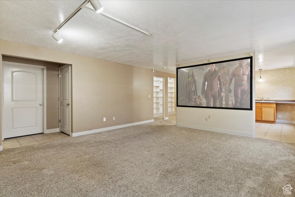 Empty room with light colored carpet, a textured ceiling, baseboards, light tile patterned floors, and rail lighting