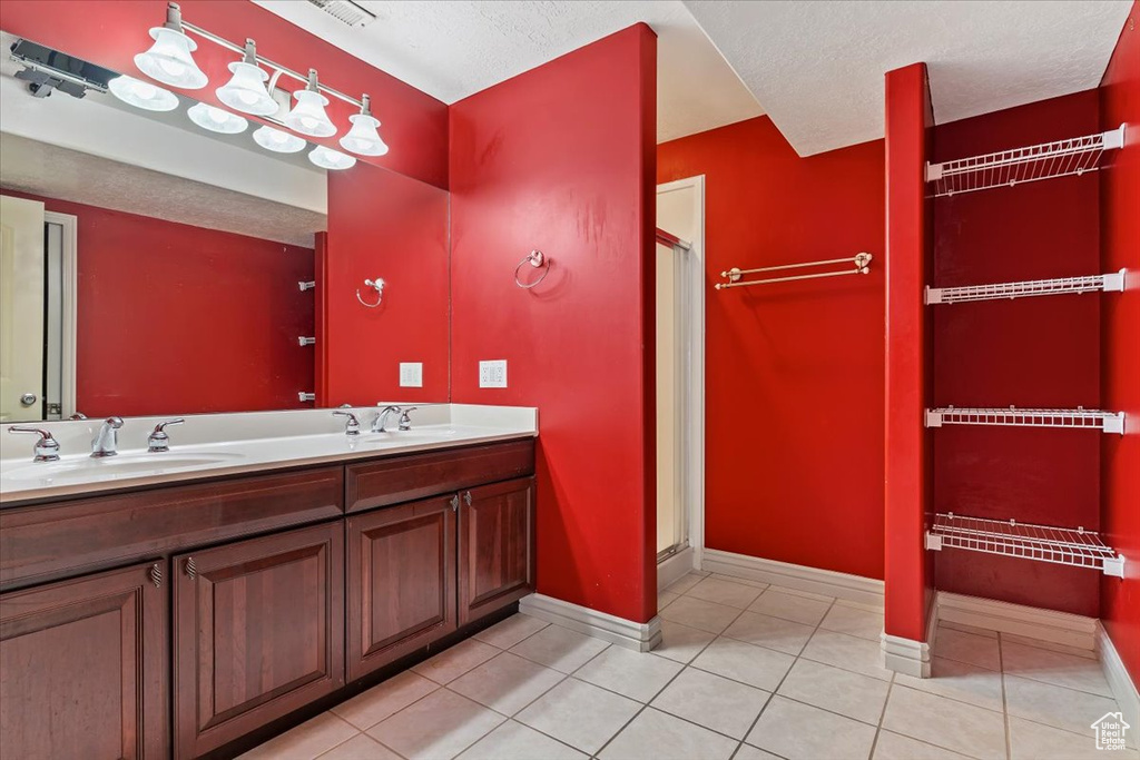 Full bathroom featuring baseboards, tile patterned floors, double vanity, a stall shower, and a textured ceiling