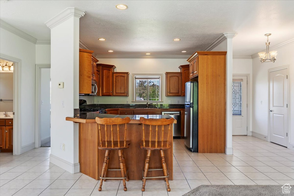 Kitchen with appliances with stainless steel finishes, a peninsula, dark countertops, a breakfast bar area, and ornamental molding
