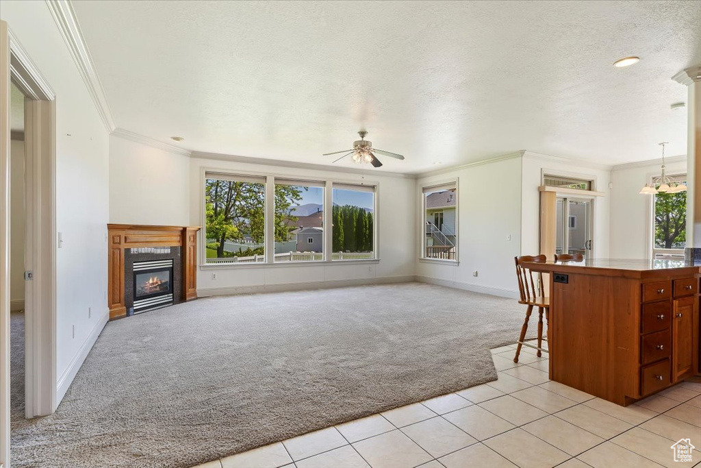 Unfurnished living room featuring light colored carpet, healthy amount of natural light, ornamental molding, a ceiling fan, and a glass covered fireplace
