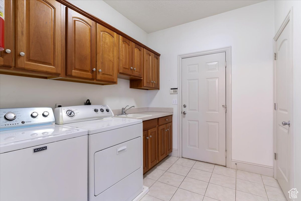 Laundry area with washer and dryer, cabinet space, light tile patterned floors, and baseboards