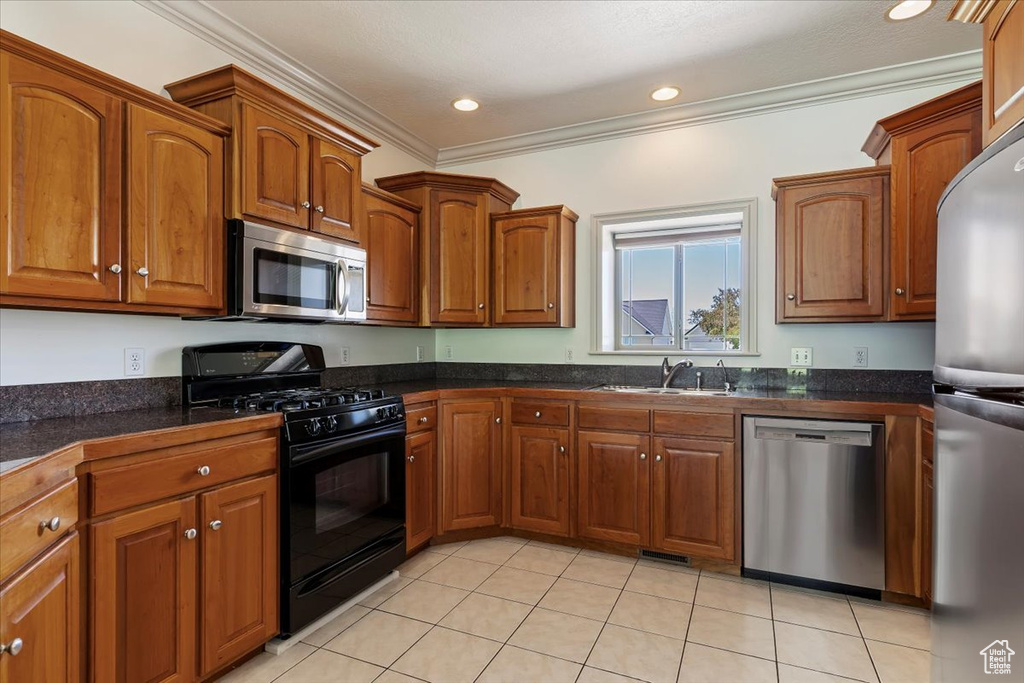 Kitchen with appliances with stainless steel finishes, a sink, ornamental molding, brown cabinets, and dark countertops