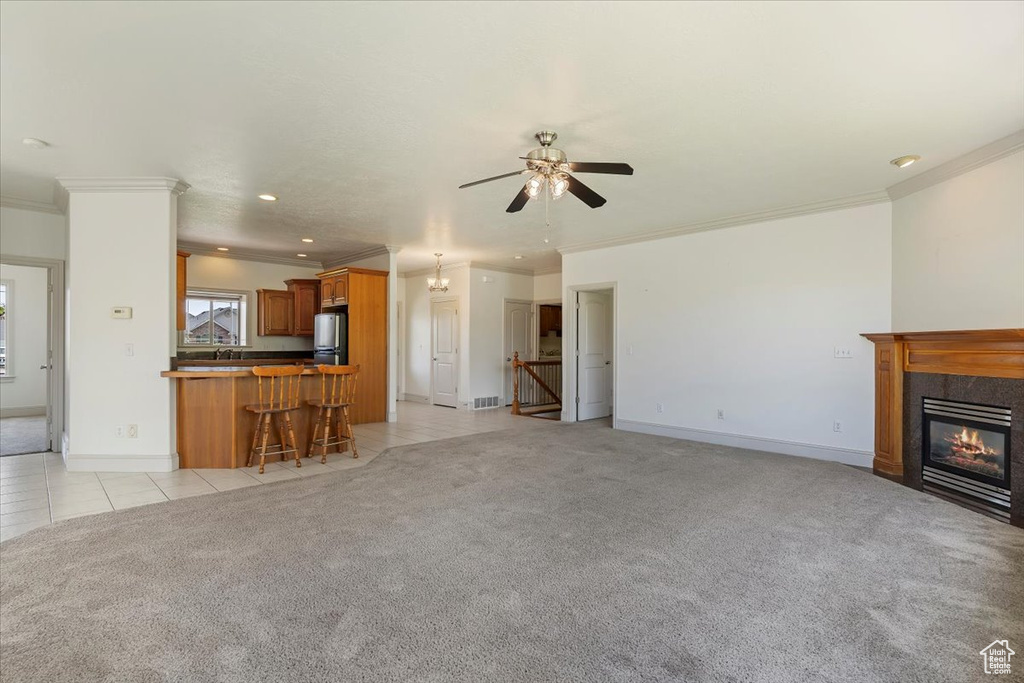 Unfurnished living room featuring light carpet, crown molding, a ceiling fan, a glass covered fireplace, and baseboards