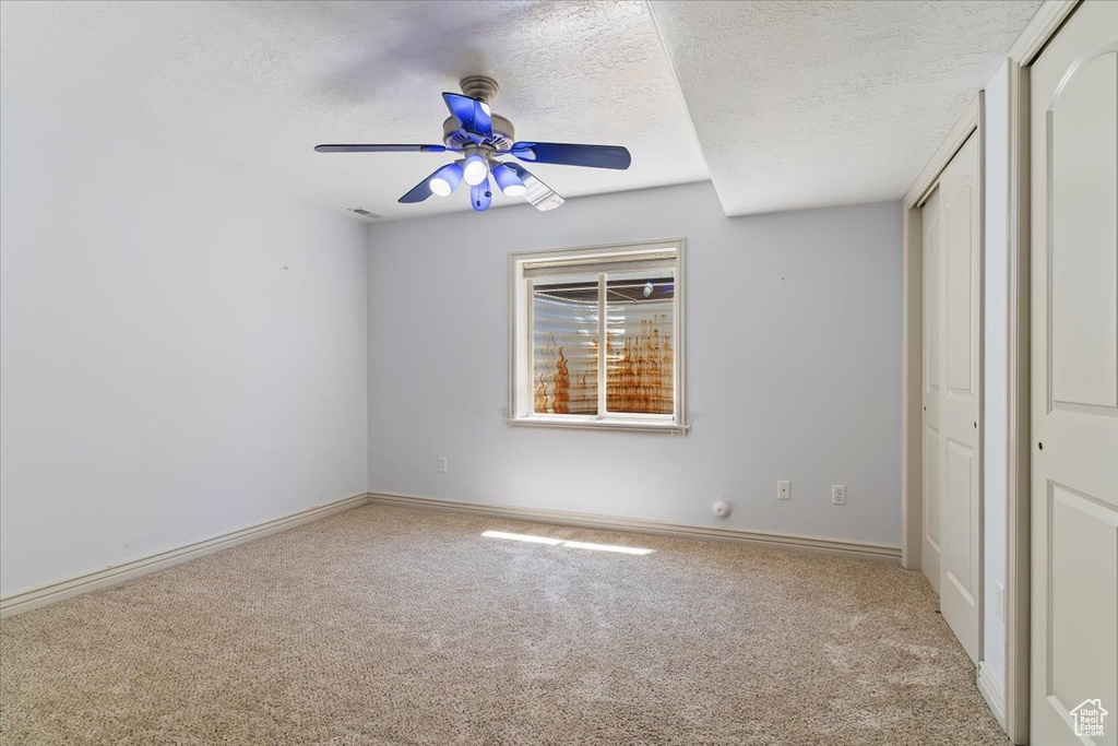 Unfurnished bedroom with carpet, a textured ceiling, baseboards, a ceiling fan, and a closet