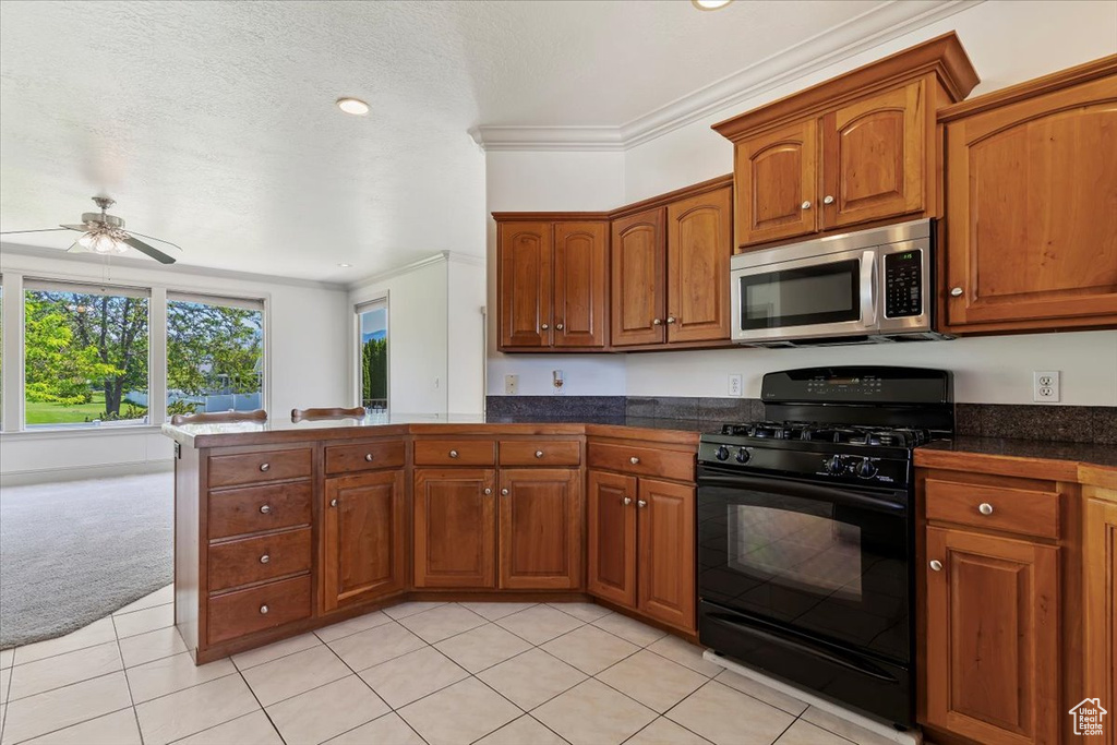 Kitchen featuring stainless steel microwave, black range with gas stovetop, a peninsula, ornamental molding, and brown cabinets