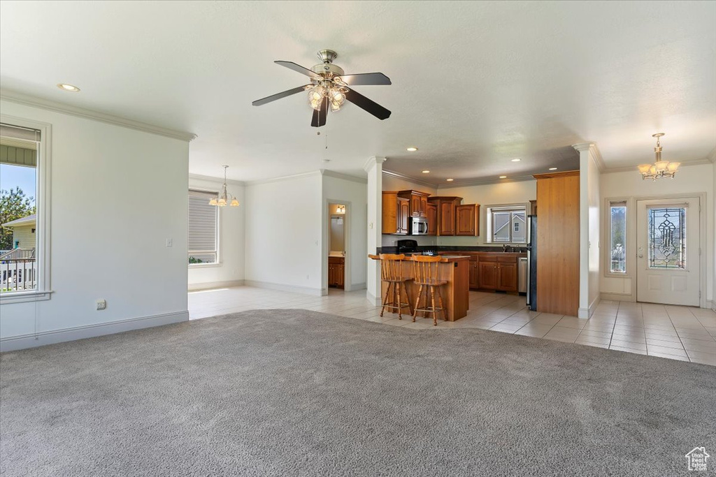 Unfurnished living room featuring a chandelier, light carpet, healthy amount of natural light, light tile patterned flooring, and ornamental molding