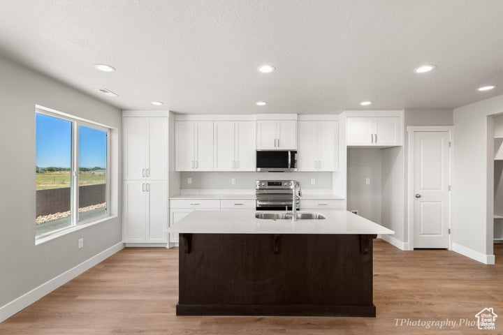 Kitchen featuring appliances with stainless steel finishes, a sink, baseboards, light countertops, and white cabinets