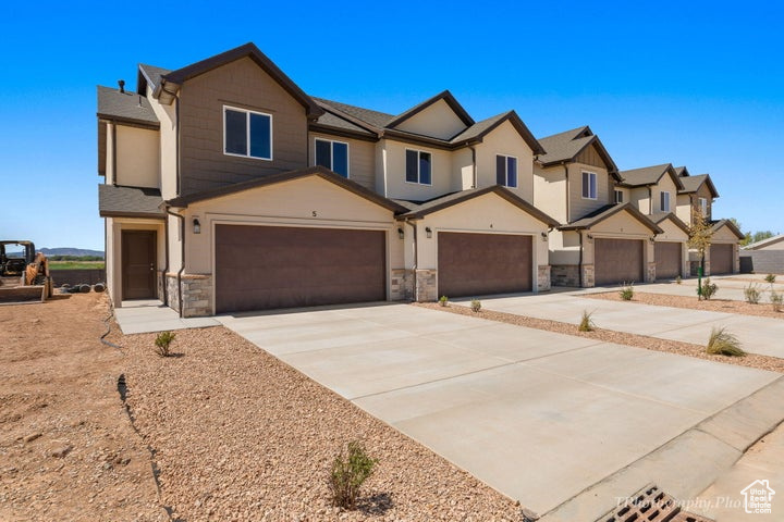Multi unit property with a garage, stone siding, concrete driveway, and a residential view